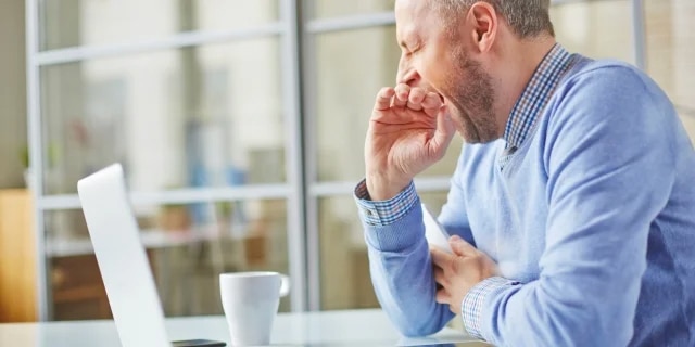 man yawning looking at his laptop