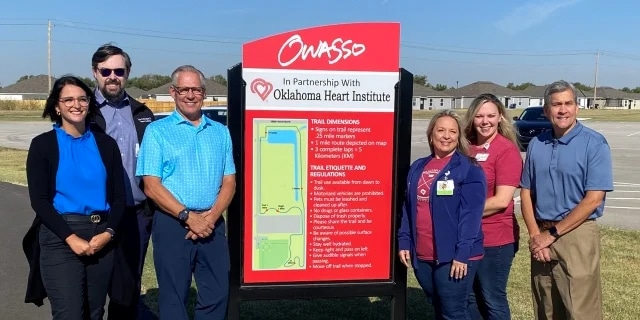 Six people next to a trail head sign with the OK Heart Institute logo at the top of it